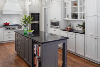 Example of a large trendy u-shaped medium tone wood floor and brown floor open concept kitchen design in Philadelphia with a farmhouse sink, flat-panel cabinets, white cabinets, quartz countertops, beige backsplash, marble backsplash, stainless steel appliances, an island and black countertops