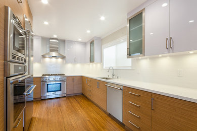 Example of a large trendy l-shaped medium tone wood floor and brown floor kitchen design in San Francisco with an undermount sink, flat-panel cabinets, white cabinets, quartz countertops, white backsplash, stainless steel appliances and no island