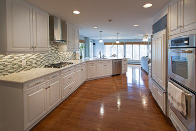 Example of a large trendy galley dark wood floor and brown floor enclosed kitchen design in New York with a double-bowl sink, raised-panel cabinets, white cabinets, marble countertops, multicolored backsplash, mosaic tile backsplash, paneled appliances and a peninsula
