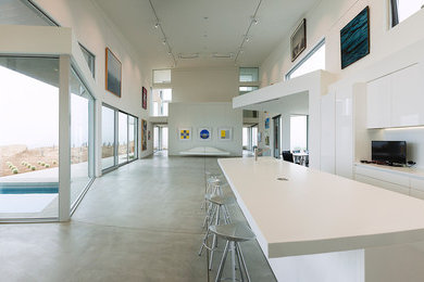 Einzeilige, Große Moderne Wohnküche mit flächenbündigen Schrankfronten, weißen Schränken, Küchenrückwand in Weiß, weißen Elektrogeräten, Betonboden und Kücheninsel in San Diego