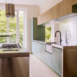 Inspiration pour une cuisine américaine design avec un évier de ferme, des portes de placard turquoises, un plan de travail en inox, une crédence métallisée, un électroménager en acier inoxydable, un sol en bois clair et un îlot central.
