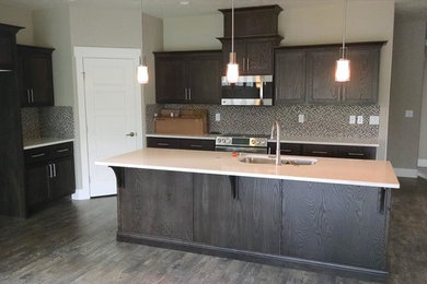Inspiration for a mid-sized contemporary l-shaped medium tone wood floor open concept kitchen remodel in Boise with a double-bowl sink, shaker cabinets, dark wood cabinets, quartzite countertops, black backsplash, stainless steel appliances and an island