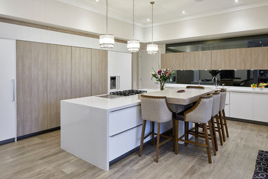 Design ideas for a large modern l-shaped kitchen/diner in London with a double-bowl sink, flat-panel cabinets, light wood cabinets, quartz worktops, grey splashback, mirror splashback, stainless steel appliances, porcelain flooring, an island, brown floors and white worktops.