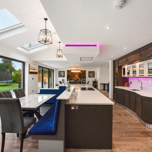 Expansive contemporary galley kitchen/diner in London with a submerged sink, shaker cabinets, medium wood cabinets, white splashback, stainless steel appliances, an island, brown floors and beige worktops.