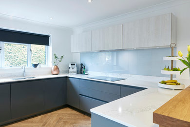 This is an example of a medium sized contemporary u-shaped kitchen/diner in Devon with a built-in sink, flat-panel cabinets, grey cabinets, quartz worktops, grey splashback, glass sheet splashback, integrated appliances, lino flooring and a breakfast bar.