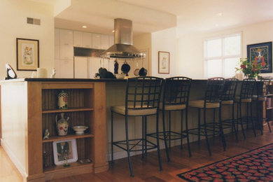 Photo of a large traditional u-shaped kitchen/diner in Manchester with a submerged sink, flat-panel cabinets, white cabinets, stainless steel worktops, stainless steel appliances, medium hardwood flooring, an island and brown floors.