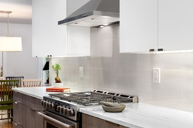 Inredning av ett modernt mellanstort vit vitt kök, med en undermonterad diskho, släta luckor, vita skåp, bänkskiva i kvarts, grått stänkskydd, stänkskydd i porslinskakel, rostfria vitvaror, laminatgolv och grått golv