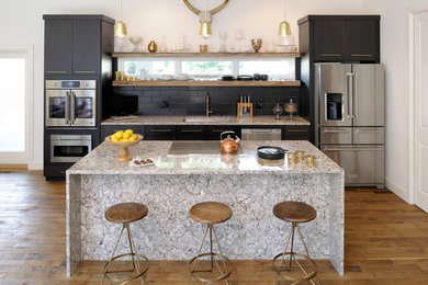 Example of a trendy single-wall medium tone wood floor open concept kitchen design in St Louis with an undermount sink, flat-panel cabinets, black cabinets, black backsplash, subway tile backsplash, stainless steel appliances, an island, granite countertops and gray countertops