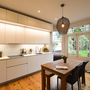 Photo of a medium sized contemporary l-shaped kitchen/diner in London with flat-panel cabinets, white cabinets, quartz worktops, stainless steel appliances, no island, white worktops, a submerged sink, medium hardwood flooring and brown floors.