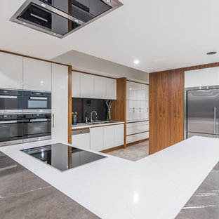 Contemporary u-shaped kitchen in Perth with a drop-in sink, flat-panel cabinets, white cabinets, black splashback, glass sheet splashback, stainless steel appliances, with island, grey floor and white benchtop.