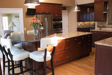 Eat-in kitchen - mid-sized traditional l-shaped medium tone wood floor eat-in kitchen idea in Cincinnati with an undermount sink, recessed-panel cabinets, dark wood cabinets, granite countertops, beige backsplash, stone tile backsplash, stainless steel appliances and an island