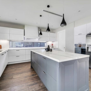 Design ideas for a contemporary u-shaped kitchen in Sydney with a double-bowl sink, flat-panel cabinets, white cabinets, white splashback, stainless steel appliances, medium hardwood floors, with island, brown floor and white benchtop.