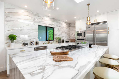 Mid-sized minimalist l-shaped porcelain tile and brown floor eat-in kitchen photo in Jacksonville with a farmhouse sink, flat-panel cabinets, white cabinets, marble countertops, white backsplash, porcelain backsplash, stainless steel appliances, an island and white countertops