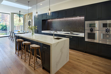 Inspiration for a large contemporary l-shaped medium tone wood floor and brown floor eat-in kitchen remodel in London with an integrated sink, recessed-panel cabinets, gray cabinets, quartzite countertops, gray backsplash, stone slab backsplash, stainless steel appliances, an island and white countertops