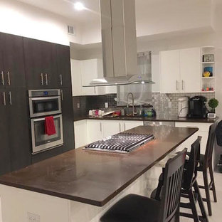 Photo of a contemporary l-shaped kitchen in New York with flat-panel cabinets, white cabinets, concrete benchtops, grey splashback, subway tile splashback, stainless steel appliances, marble floors and with island.