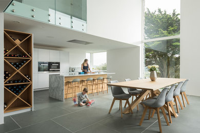 Große Moderne Wohnküche mit flächenbündigen Schrankfronten, weißen Schränken, Marmor-Arbeitsplatte, Schieferboden, grauem Boden und Kücheninsel in Cornwall