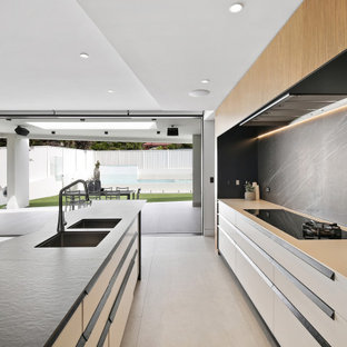This is an example of a large contemporary galley eat-in kitchen in Sydney with a double-bowl sink, flat-panel cabinets, white cabinets, black splashback, porcelain splashback, stainless steel appliances, porcelain floors, with island, grey floor and white benchtop.