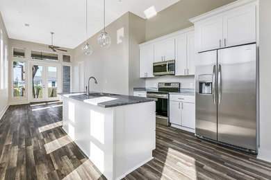 This is an example of a small contemporary single-wall open plan kitchen in New Orleans with a double-bowl sink, shaker cabinets, white cabinets, stainless steel appliances, dark hardwood flooring, an island, brown floors and grey worktops.