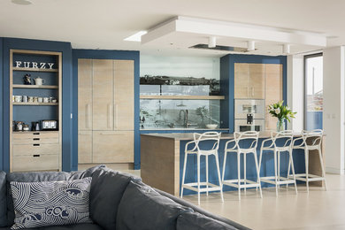Large contemporary single-wall open plan kitchen in Cornwall with a built-in sink, flat-panel cabinets, medium wood cabinets, quartz worktops, multi-coloured splashback, glass sheet splashback, integrated appliances, concrete flooring, an island, beige floors and beige worktops.