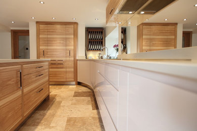 Inspiration for a medium sized modern l-shaped kitchen/diner in Manchester with a submerged sink, flat-panel cabinets, light wood cabinets, engineered stone countertops, glass sheet splashback, stainless steel appliances and travertine flooring.