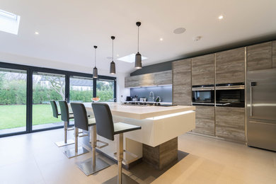 Design ideas for a medium sized contemporary single-wall kitchen in London with flat-panel cabinets, grey splashback, stainless steel appliances, an island and beige floors.