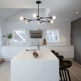 Design ideas for a contemporary u-shaped enclosed kitchen in London with a submerged sink, flat-panel cabinets, white cabinets, marble worktops, white splashback, marble splashback, integrated appliances, light hardwood flooring, an island, beige floors and white worktops.
