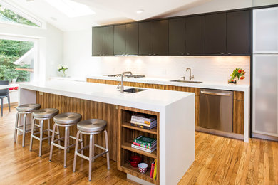 Example of a trendy galley medium tone wood floor kitchen design in DC Metro with an undermount sink, flat-panel cabinets, medium tone wood cabinets, white backsplash, porcelain backsplash and an island