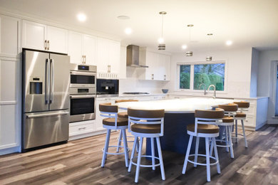 Large contemporary l-shaped kitchen/diner in Vancouver with a submerged sink, flat-panel cabinets, white cabinets, engineered stone countertops, white splashback, ceramic splashback, stainless steel appliances, vinyl flooring, an island, brown floors and white worktops.