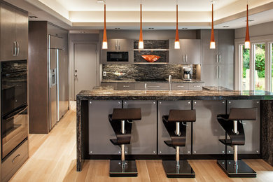 Example of a mid-sized trendy u-shaped light wood floor and beige floor open concept kitchen design in Omaha with flat-panel cabinets, granite countertops, stone slab backsplash, black appliances, an island, gray cabinets and multicolored backsplash