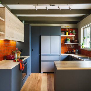 Mid-sized contemporary u-shaped eat-in kitchen in Melbourne with a double-bowl sink, flat-panel cabinets, laminate benchtops, orange splashback, ceramic splashback, black appliances, medium hardwood floors, a peninsula and exposed beam.