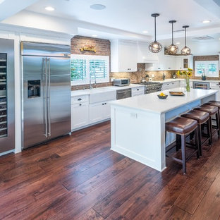 Photo of a mid-sized contemporary l-shaped eat-in kitchen in Los Angeles with a farmhouse sink, shaker cabinets, white cabinets, quartz benchtops, red splashback, brick splashback, stainless steel appliances, dark hardwood floors and with island.