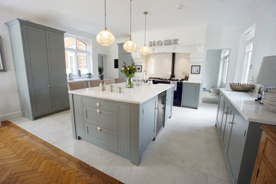 Photo of a large traditional u-shaped kitchen in Kent with a belfast sink, shaker cabinets, grey cabinets, quartz worktops, black appliances, light hardwood flooring, an island, brown floors and white worktops.