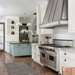 Foto di una cucina mediterranea con ante lisce, ante bianche, paraspruzzi bianco, paraspruzzi con piastrelle diamantate, elettrodomestici in acciaio inossidabile, pavimento in terracotta e isola