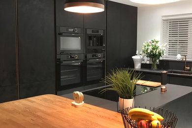 Inredning av ett modernt mellanstort svart svart kök och matrum, med en integrerad diskho, släta luckor, svarta skåp, bänkskiva i kvarts, svarta vitvaror, klinkergolv i porslin, en köksö och vitt golv