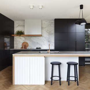 This is an example of a contemporary l-shaped open plan kitchen in Adelaide with an undermount sink, black cabinets, marble benchtops, white splashback, marble splashback, black appliances, light hardwood floors, with island and white benchtop.