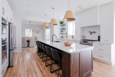 Eat-in kitchen - large contemporary galley light wood floor and brown floor eat-in kitchen idea in Milwaukee with an undermount sink, shaker cabinets, white cabinets, quartz countertops, white backsplash, subway tile backsplash, stainless steel appliances, an island and white countertops
