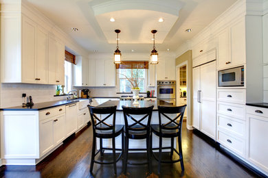 Eat-in kitchen - large contemporary u-shaped dark wood floor and brown floor eat-in kitchen idea in New York with a farmhouse sink, shaker cabinets, white cabinets, solid surface countertops, white backsplash, subway tile backsplash, stainless steel appliances and an island