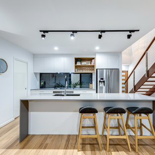 Photo of a mid-sized contemporary galley eat-in kitchen in Sunshine Coast with an undermount sink, flat-panel cabinets, white cabinets, window splashback, stainless steel appliances, light hardwood floors, with island, beige floor, grey benchtop and quartz benchtops.