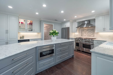 Large trendy l-shaped dark wood floor and brown floor eat-in kitchen photo in Atlanta with an undermount sink, recessed-panel cabinets, white cabinets, quartz countertops, white backsplash, ceramic backsplash, stainless steel appliances and an island
