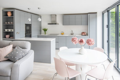 This is an example of a medium sized contemporary u-shaped open plan kitchen in Devon with a submerged sink, flat-panel cabinets, grey cabinets, composite countertops, a breakfast bar and white worktops.