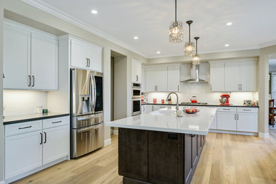 Inspiration for a large contemporary l-shaped light wood floor and brown floor open concept kitchen remodel in San Diego with a farmhouse sink, shaker cabinets, white cabinets, quartz countertops, white backsplash, ceramic backsplash, stainless steel appliances, an island and white countertops