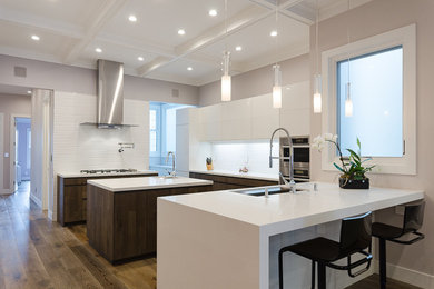 Example of a large trendy single-wall medium tone wood floor and brown floor kitchen design in San Francisco with an undermount sink, flat-panel cabinets, white cabinets, solid surface countertops, white backsplash, stainless steel appliances and an island