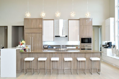 Inspiration for a large contemporary galley light wood floor and beige floor eat-in kitchen remodel in Calgary with an undermount sink, flat-panel cabinets, light wood cabinets, solid surface countertops, white backsplash, ceramic backsplash, paneled appliances, an island and brown countertops
