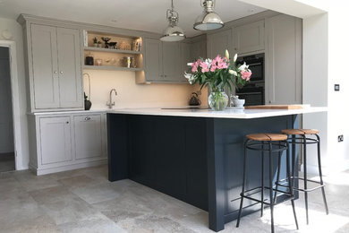 Large traditional l-shaped kitchen/diner in Gloucestershire with an integrated sink, shaker cabinets, grey cabinets, quartz worktops, white splashback, stone slab splashback, stainless steel appliances, porcelain flooring, an island, beige floors and white worktops.
