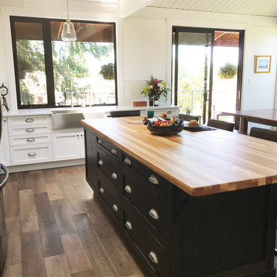 Inspiration for a large farmhouse l-shaped brown floor eat-in kitchen remodel in Vancouver with shaker cabinets, black cabinets, white backsplash, stainless steel appliances, an island, a farmhouse sink, wood countertops, ceramic backsplash and brown countertops