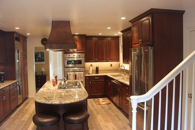 Bild på ett mellanstort vintage kök, med en dubbel diskho, luckor med upphöjd panel, skåp i mellenmörkt trä, granitbänkskiva, grått stänkskydd, stänkskydd i keramik, rostfria vitvaror, ljust trägolv och en köksö
