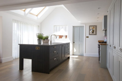 This is an example of a medium sized country kitchen in Berkshire with shaker cabinets, grey cabinets, composite countertops, grey splashback, medium hardwood flooring, an island and grey floors.