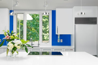 Example of a mid-sized eclectic l-shaped ceramic tile and gray floor eat-in kitchen design in Other with an undermount sink, flat-panel cabinets, white cabinets, solid surface countertops, blue backsplash, glass sheet backsplash, stainless steel appliances and an island