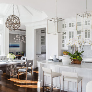 This is an example of a transitional eat-in kitchen in San Francisco with an undermount sink, glass-front cabinets, white cabinets, white splashback, panelled appliances, medium hardwood floors and with island.