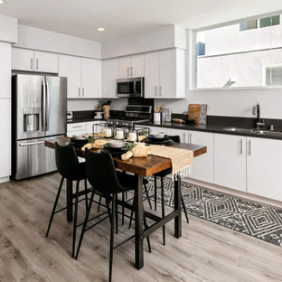 Scandinavian kitchen designs - Inspiration for a scandinavian l-shaped brown floor kitchen remodel in San Diego with a double-bowl sink, flat-panel cabinets, white cabinets, stainless steel appliances, an island and black countertops